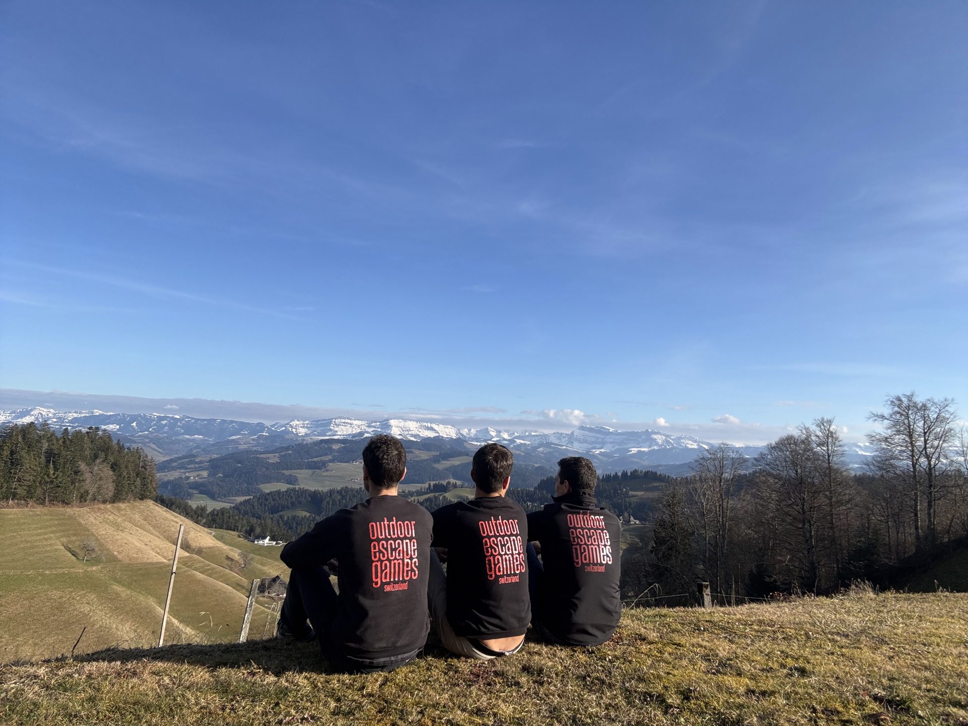 Trois membres de l'équipe Outdoor Escape Games de dos, face aux Alpes enneigées